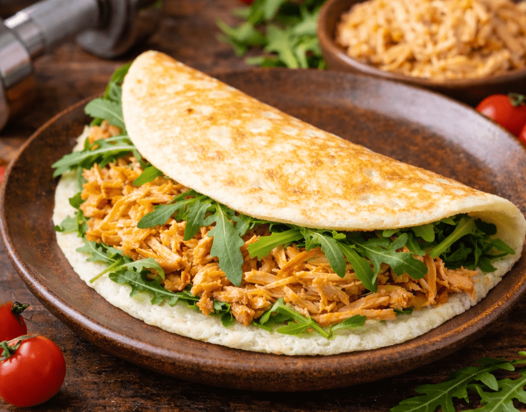 Crepioca fit de frango dobrada em um prato branco com temperos verdes