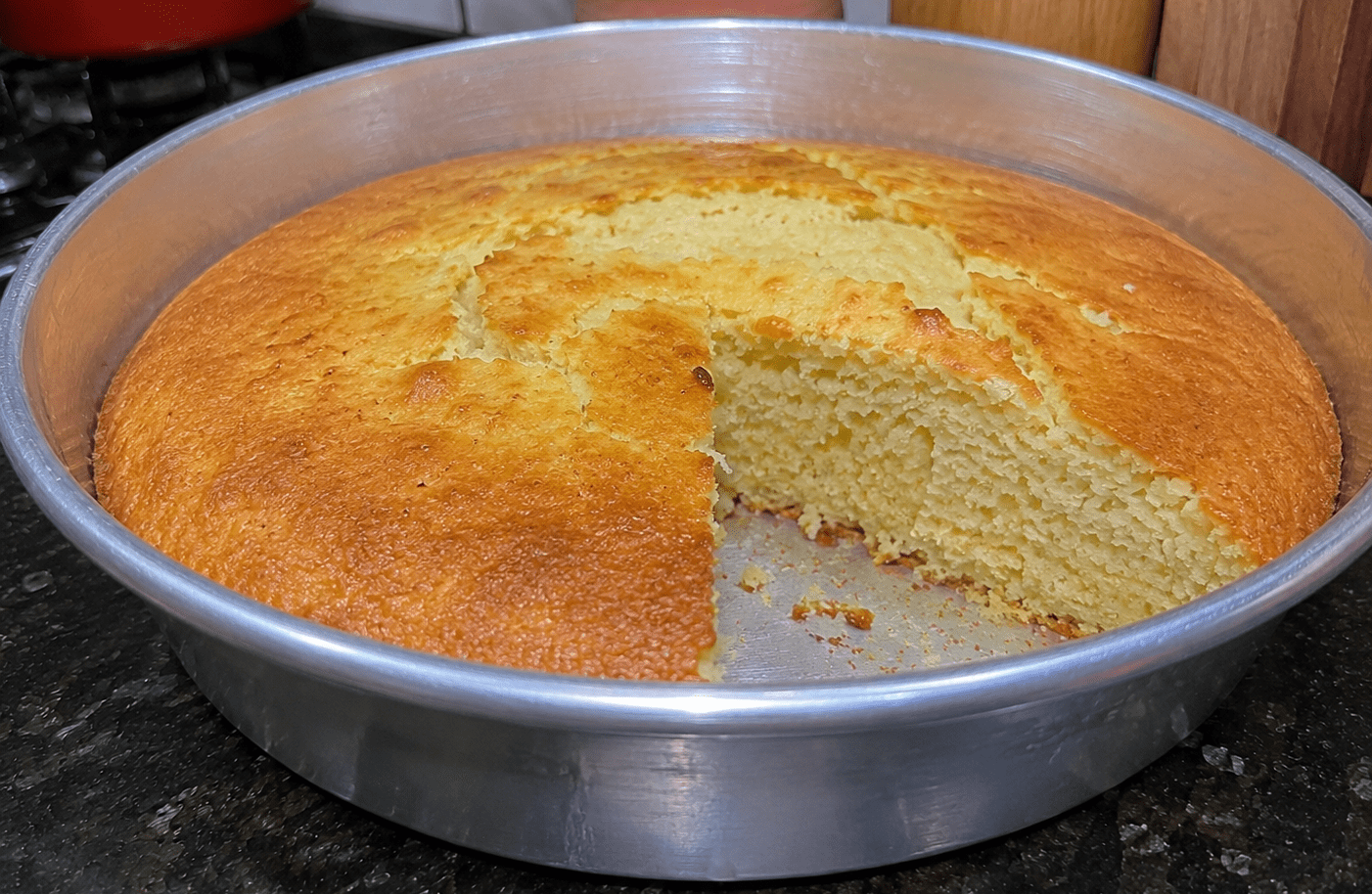 Bolo de bacia simples dourado e fofinho servido em um prato de vidro com uma xícara de café ao fundo