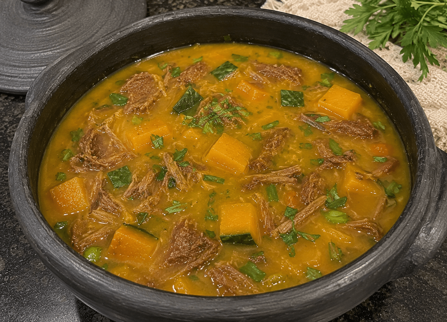 Caldo de abóbora cabotiá com carne seca cremoso e alaranjado servido em uma tigela de cerâmica com couve frita e carne seca desfiada por cima
