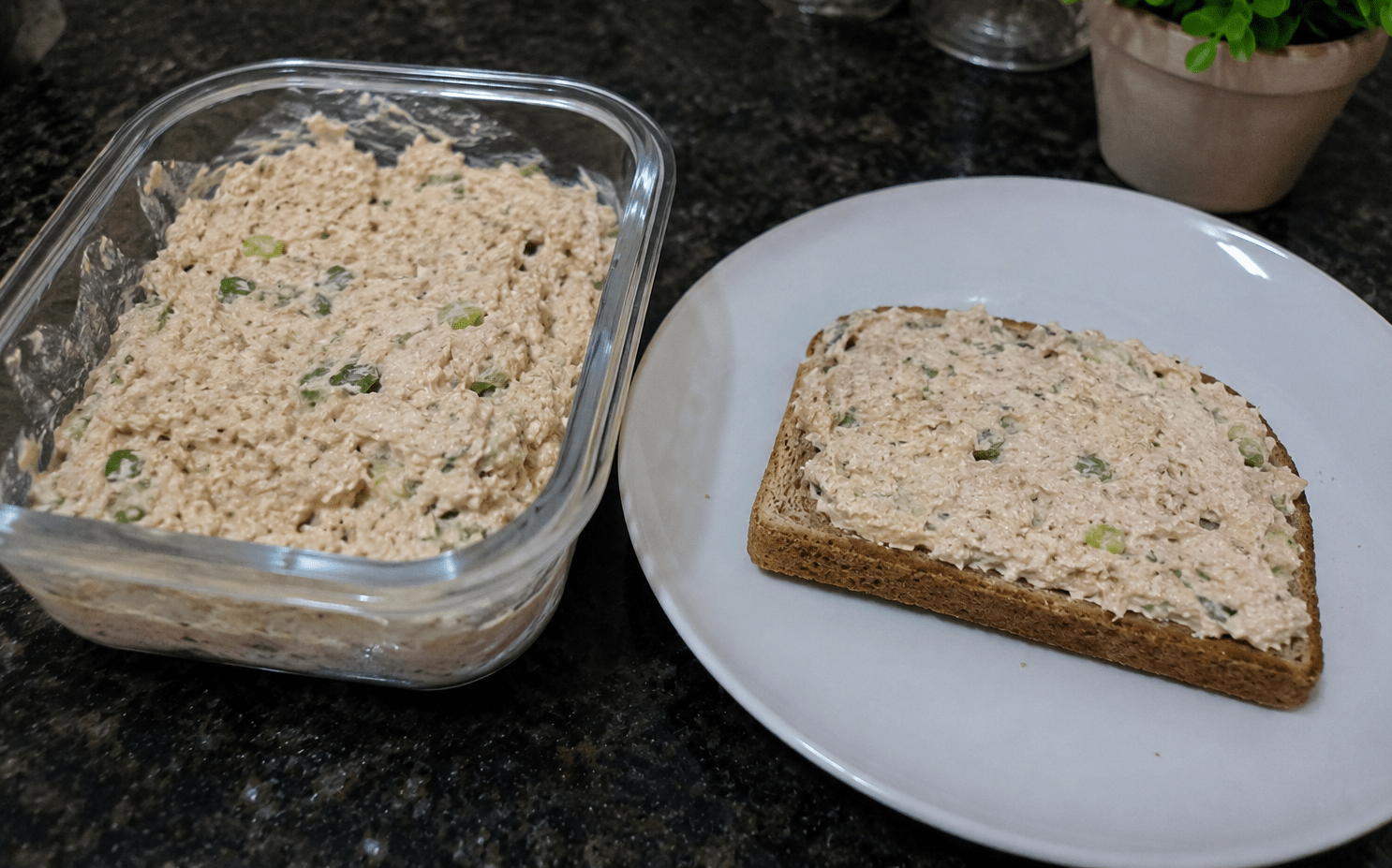Patê de atum cremoso servido em uma tigela branca cercado por fatias de pão de forma e legumes frescos